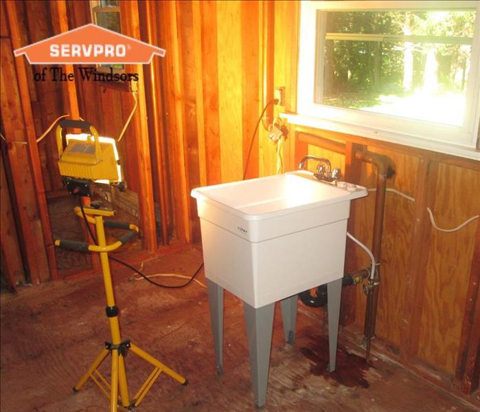 Wood Framing of a kitchen, white temporary sink in front of window SERVPRO of The Windsors Logo