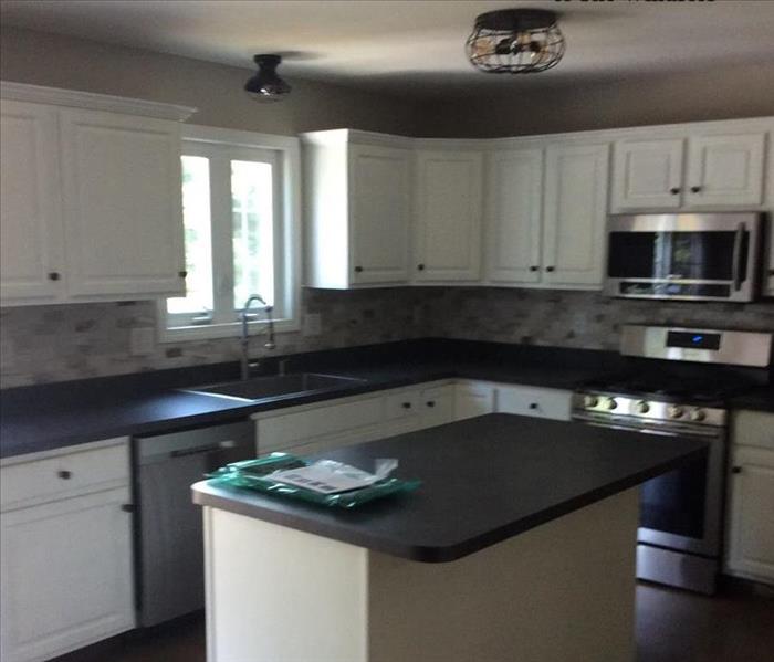 Kitchen post repair work, island and counters that are white with black counters, dark wood floors
