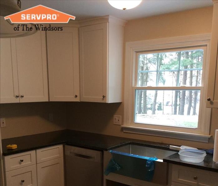 Kitchen with white cabinetry Black counter tops and Stainless steel appliances SERVPRO of The Windsors Logo