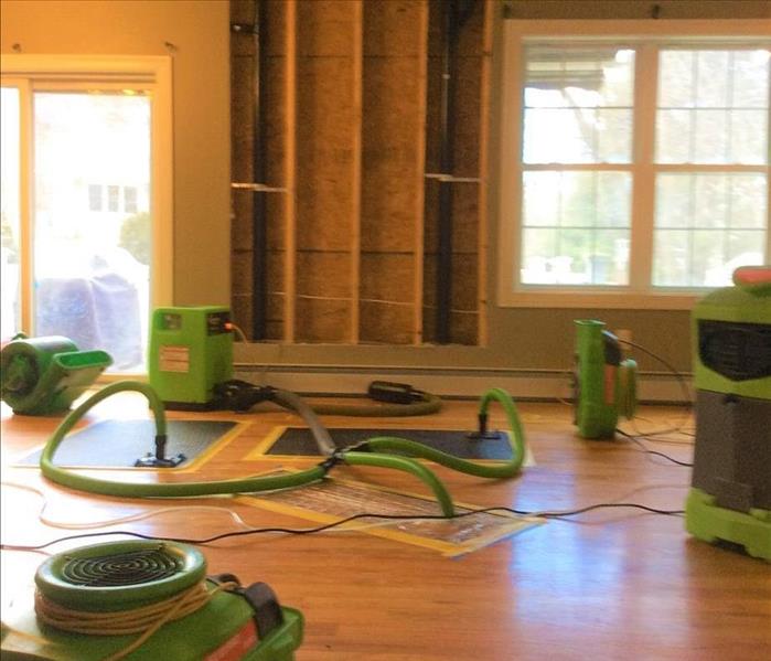 Room with drywall wall and ceiling removed, wood floors, drying equipment in place, servpro logo