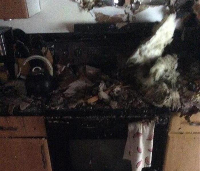 Kitchen fire, stove covered in debris, broken wall with insulation hanging out, and customers belongings destroyed by fire