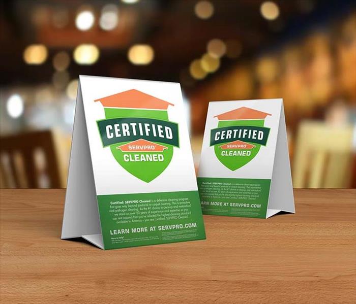 Table tent signs describing the Certified: SERVPRO Cleaned program on top of a wooden table.