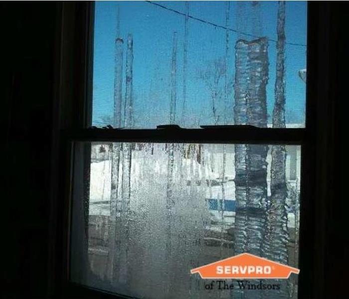 Window that has been iced over, large icicles hanging outside of window, SERVPRO of The Windsors logo